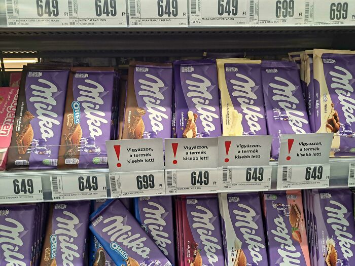 Shelves stocked with Milka chocolate bars with warning signs about reduced product size, a business solving a problem.