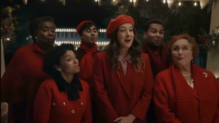A diverse group of people, all wearing red attire and some with red berets, stand together smiling, reminiscent of a festive commercial.