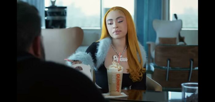 A woman with long blonde hair, wearing a Princess necklace, sitting with a drink from Dunkin'. This is one of the commercials people can't stand.