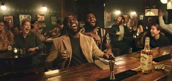 Two men laughing at a bar, enjoying a commercial people can't stand.