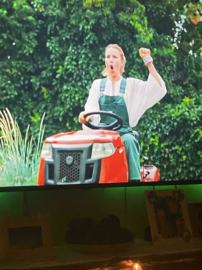 A woman in overalls enthusiastically riding a lawnmower, representing commercials people can't stand with their whole heart.