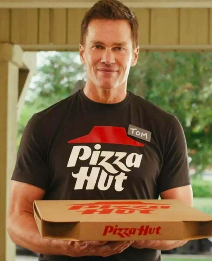 Tom Brady in a Pizza Hut uniform holds a pizza box, smiling at the camera, a memorable commercial people cant stand.