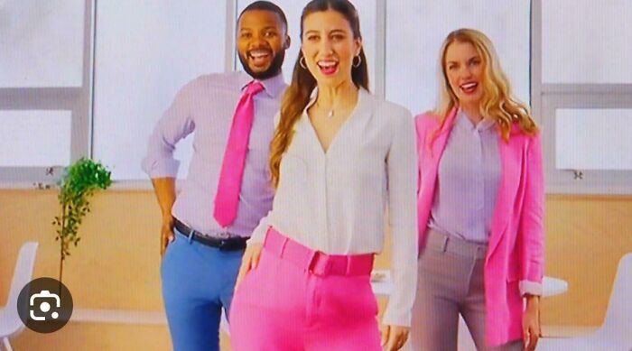 Three smiling people in business casual attire, a man in blue pants and pink tie, and two women in pink and gray outfits. This is one of the commercials people can't stand.
