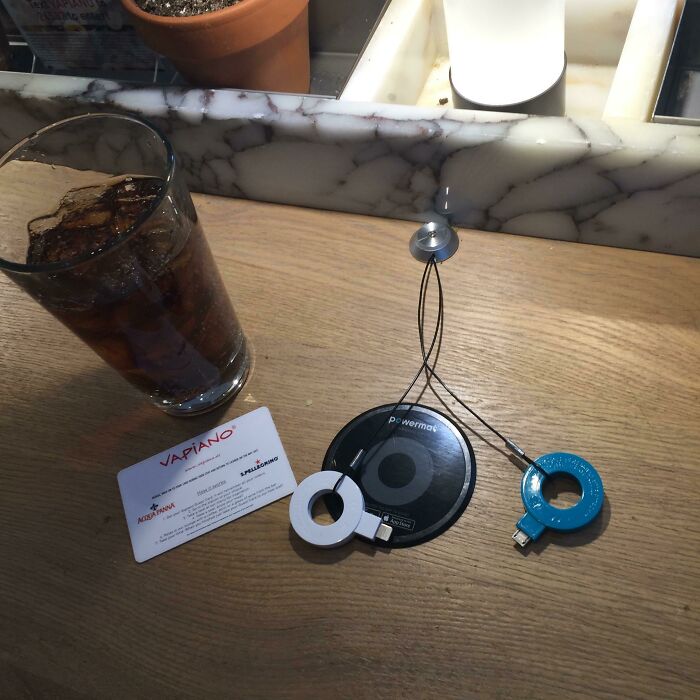 A wireless phone charger next to a drink and Vapiano card, a business solving everyday problems with genius ideas.