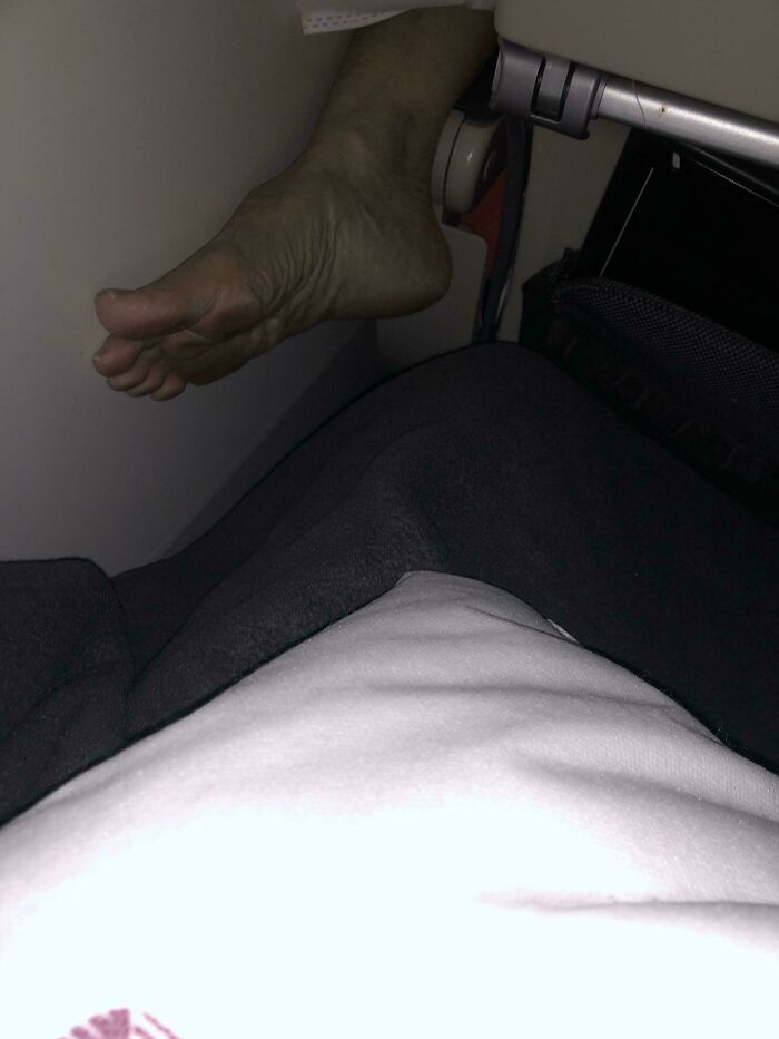 A person's bare foot resting on an airplane armrest, showcasing behavior of people who think they're the main character.