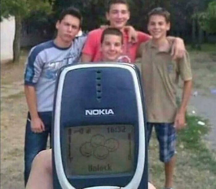 A blursed meme showing a group of boys posing for a photo, with a Nokia phone held up in the foreground displaying 'Unlock'.