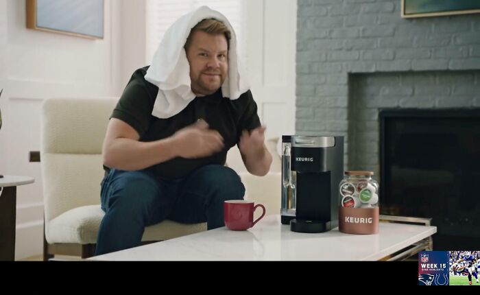 Comedian James Corden with a towel on his head, sitting next to a Keurig coffee maker, in one of the commercials people can't stand.