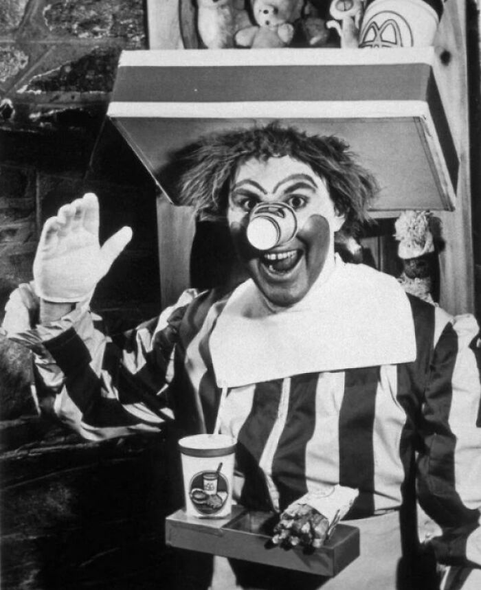 A vintage, unsettling Blursed meme of Ronald McDonald with a cup on his nose, holding a McDonald's meal.