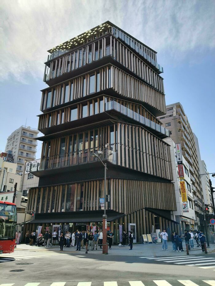 Multi-story modern architecture design building with wooden vertical slats and balconies, bustling street scene below.