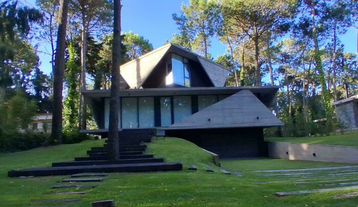 Modern architecture design: A unique angular house nestled among tall trees on a green lawn.