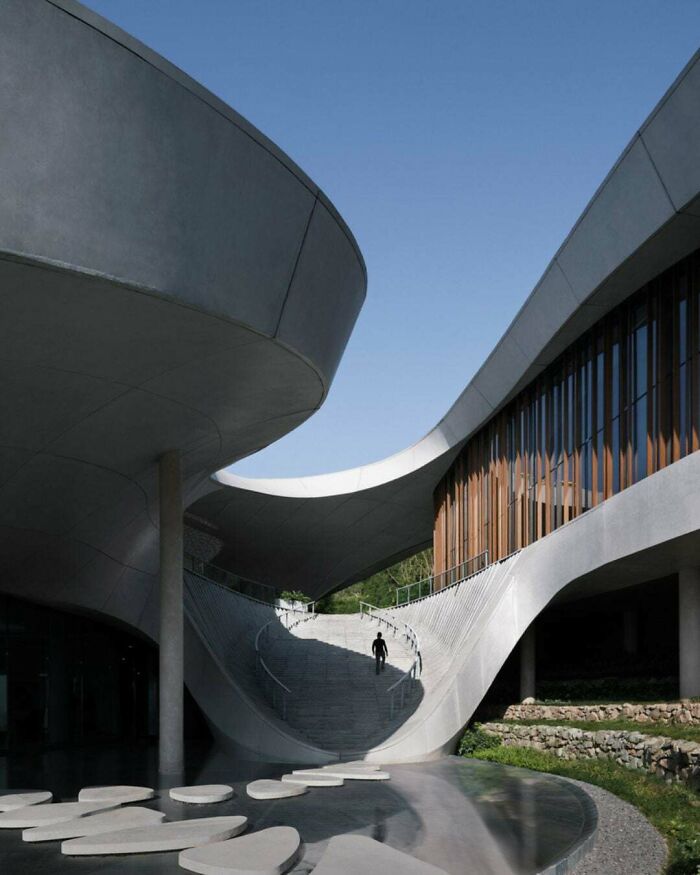 Modern architecture design: A person walking down a sweeping curved concrete staircase in a modern building.