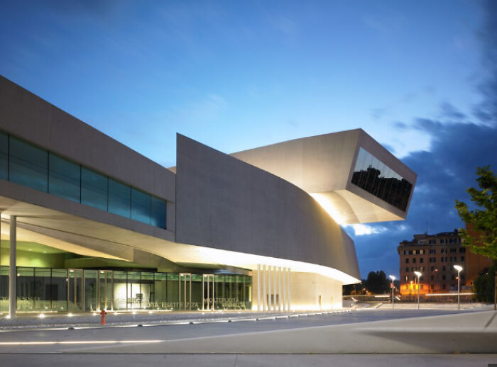 Modern architecture design: A grand, curved modern building with large windows illuminated at dusk.