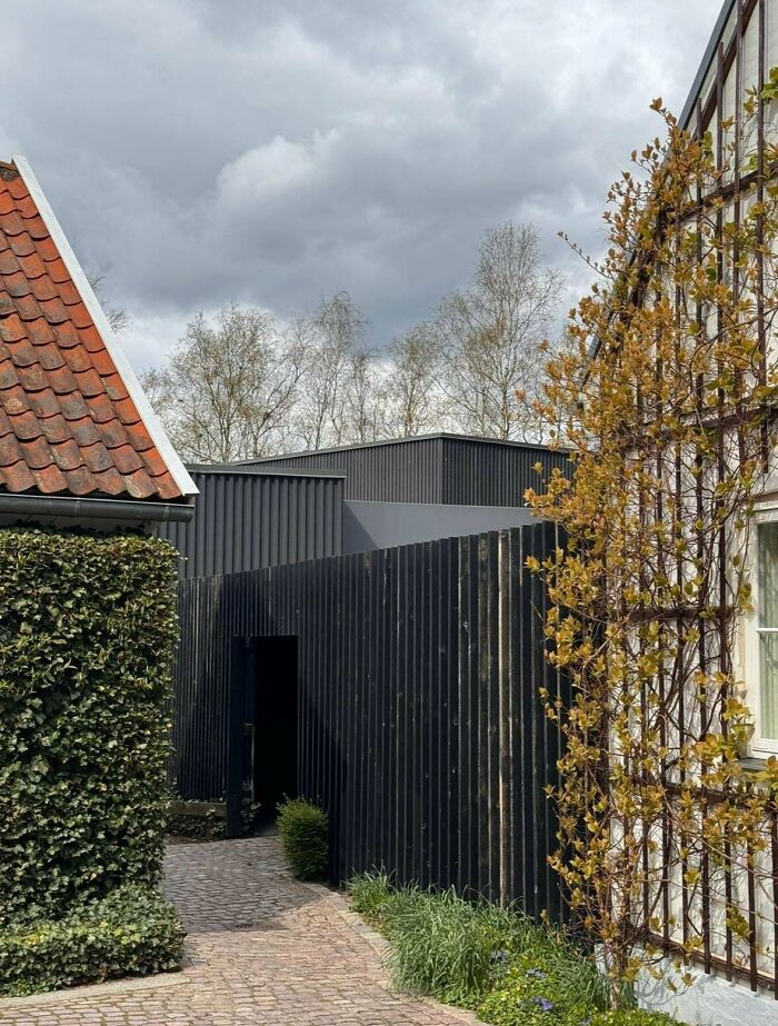 Modern architecture design: A path leading to a dark building with a red-tiled roof visible on the left.