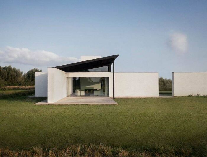 A minimalist modern architecture design house with a striking black roof and large glass facade in a green field.