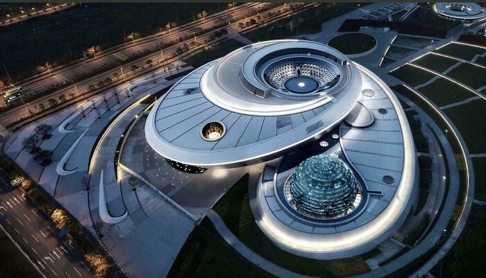 An aerial view of a stunning modern architecture design building with a circular layout and illuminated details at dusk.
