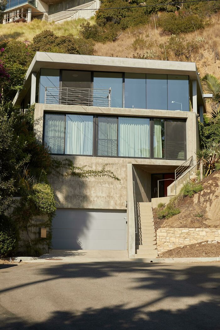 A multi-story modern architecture design house built into a hillside with large windows and a garage.