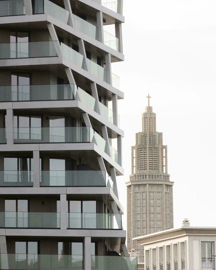 Tall modern architecture design building with angled balconies and glass railings, contrasting against an older, ornate church tower.
