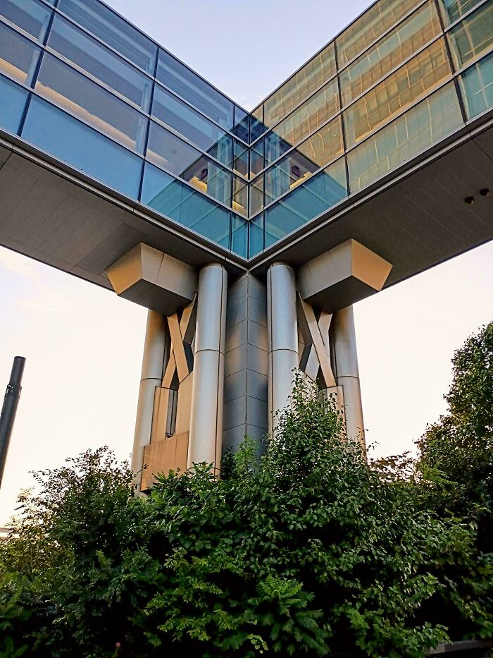 Unique modern architecture design featuring an elevated glass walkway connecting two buildings, supported by intricate columns.