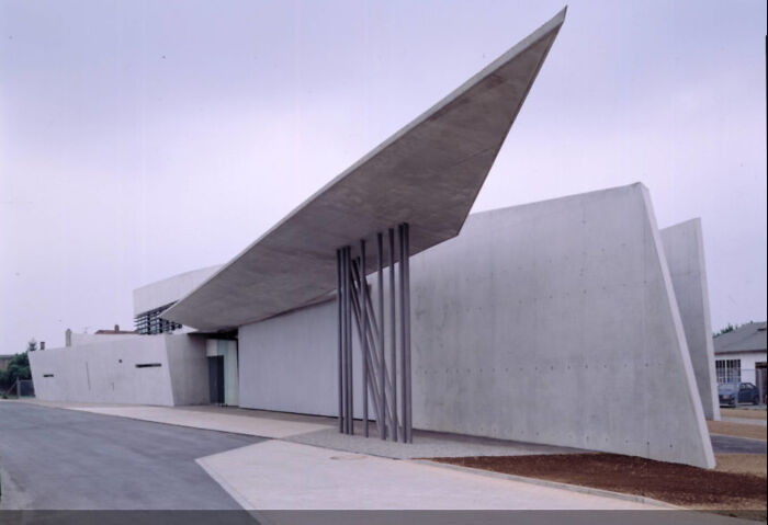 Striking modern architecture design with a sharp, angular concrete roof extending over an entrance, supported by vertical pillars.