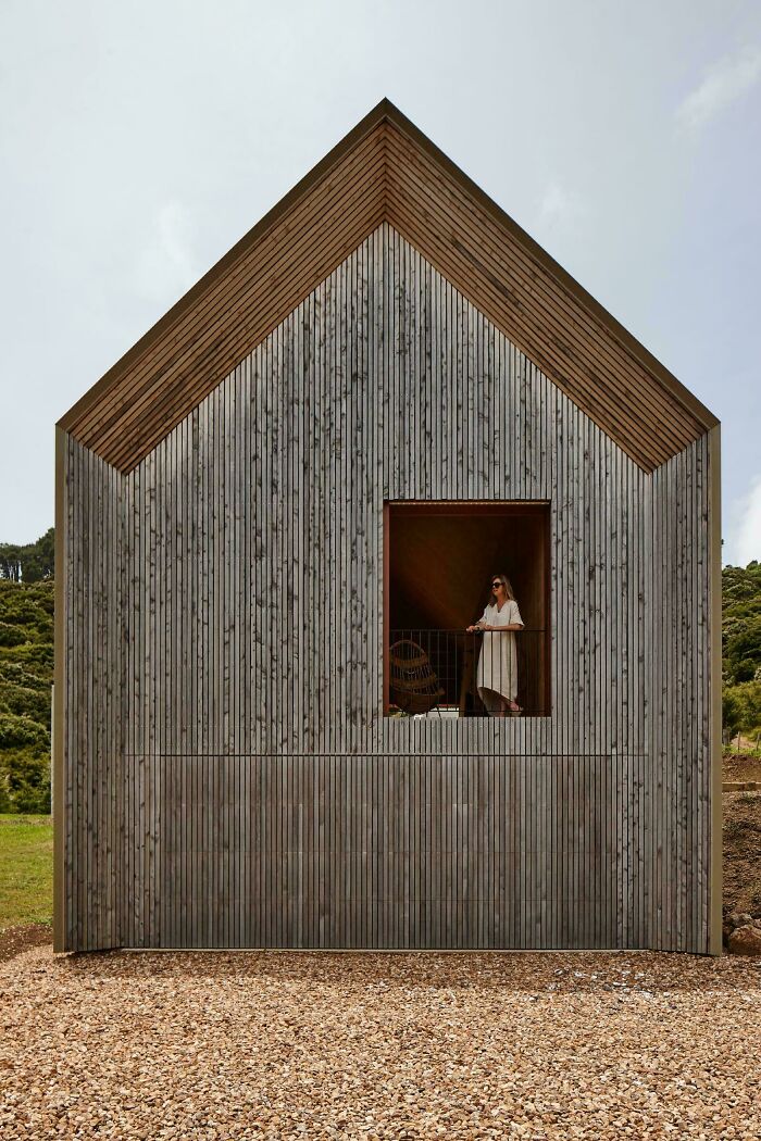 Modern architecture design of a house with vertical wooden siding and a woman standing on a balcony overlooking the landscape.