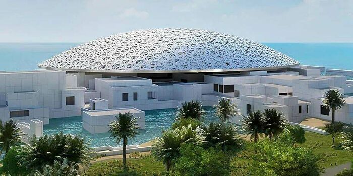 Modern architecture design of a museum with a large, intricate domed roof surrounded by water and lush greenery.