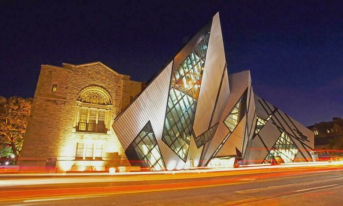 Modern architecture design of a museum with a deconstructivist facade glowing at night, surrounded by light trails from traffic.