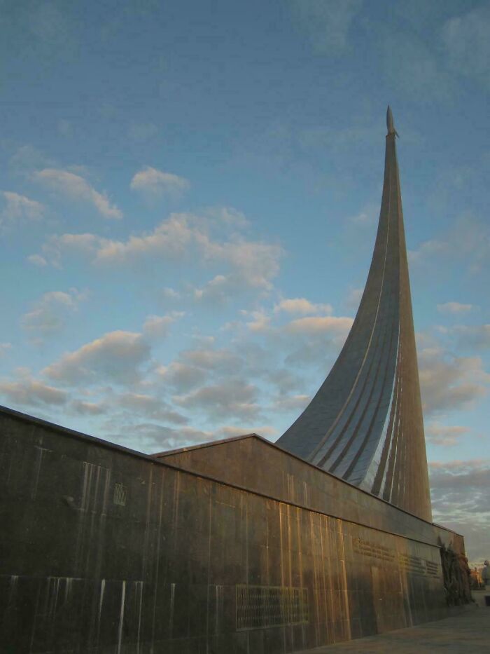 Towering modern architecture designs monument resembling a rocket, against a cloudy sky.