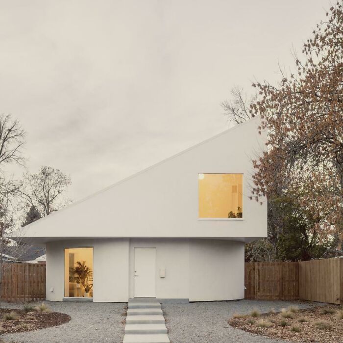 White modern architecture designs house with a distinctive sloped roof and large windows, surrounded by trees.