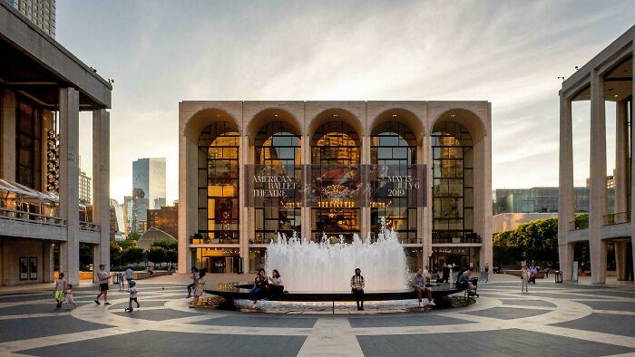 Grand modern architecture designs building with arched windows and a large fountain in a bustling public plaza.