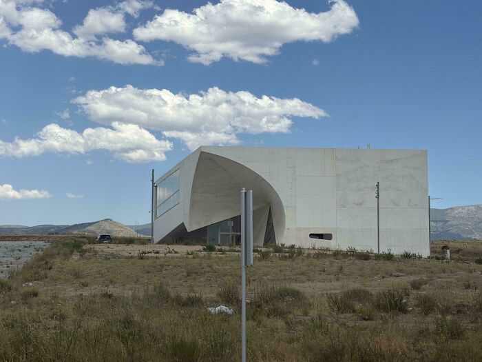 Unique modern architecture designs building with a curved concrete facade in a dry landscape.