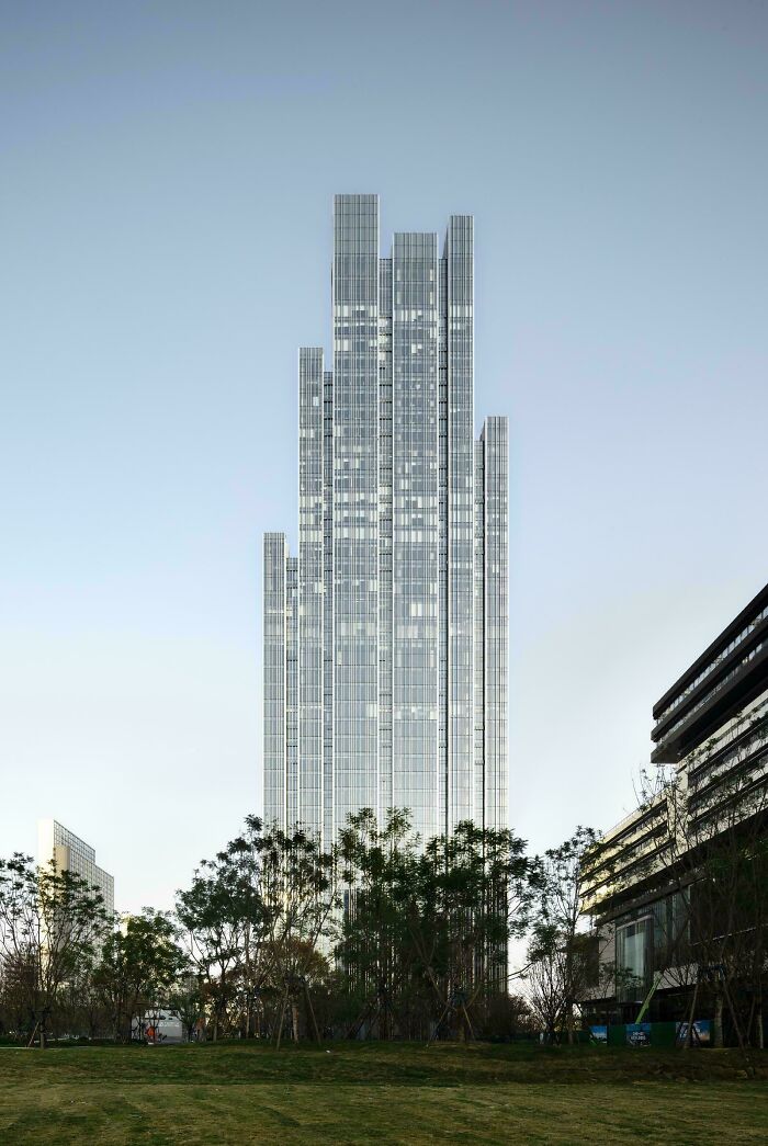 Tall, slender modern architecture designs skyscraper reaching for the sky amidst green trees.