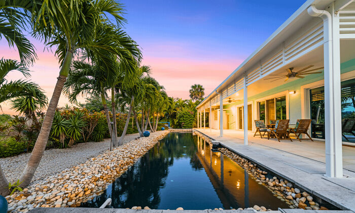 Modern Architecture Designs with a beautiful house, swimming pool, and palm trees at sunset.