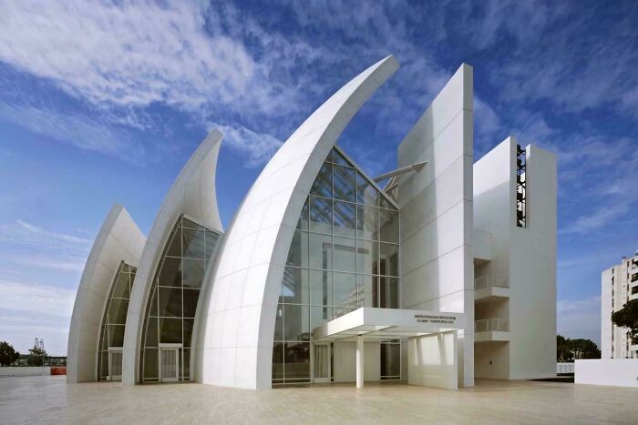 Striking modern architecture designs building featuring multiple curved white sails and glass walls.