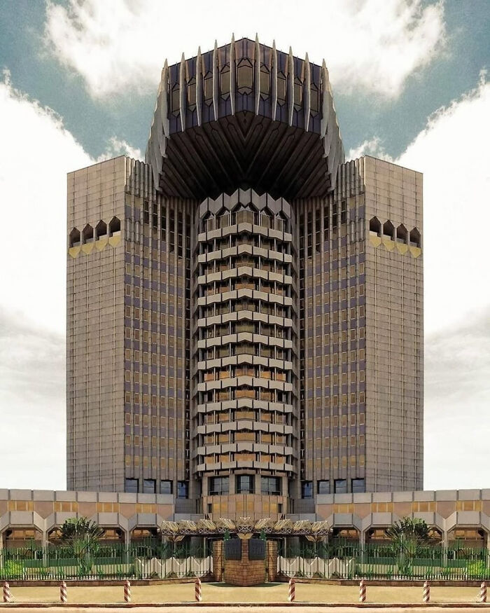 Tall, symmetrical modern architecture designs building with unique geometric patterns on its facade against a cloudy sky.