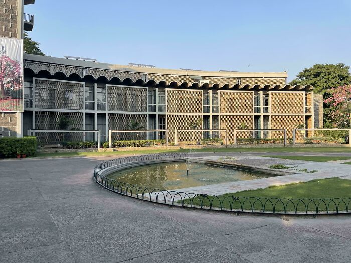 Curved modern architecture designs building with a water fountain and lush green lawn in the foreground.