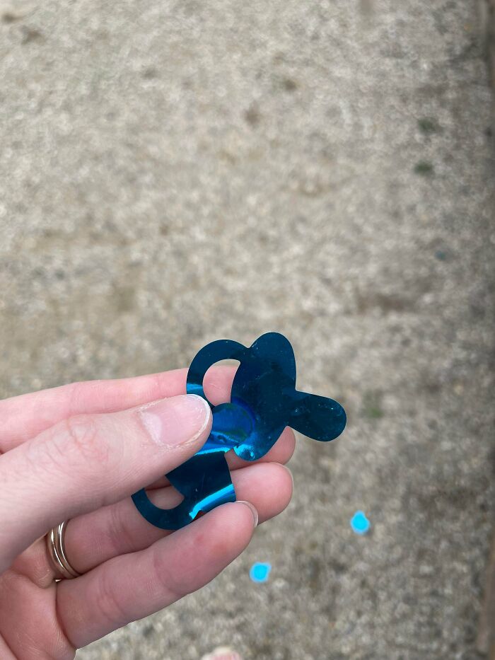 A hand holding a blue pacifier confetti cutout, a small piece from Gender Reveal moments.