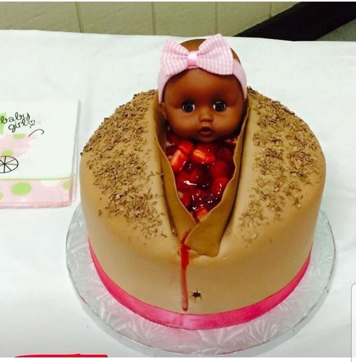 A gender reveal moment cake shaped like a doll emerging from a cake with strawberries, judged by parents.