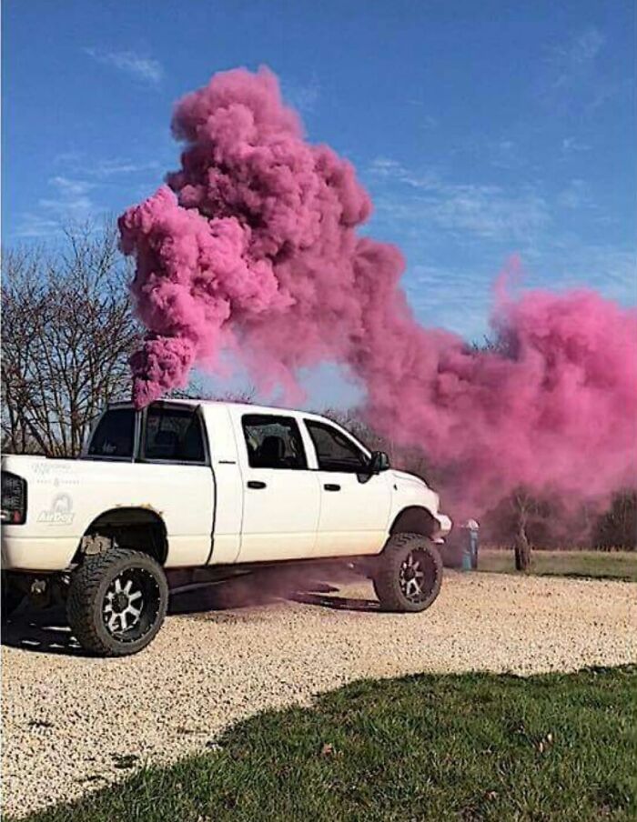 A white truck spewing a large cloud of pink smoke during a gender reveal moment.