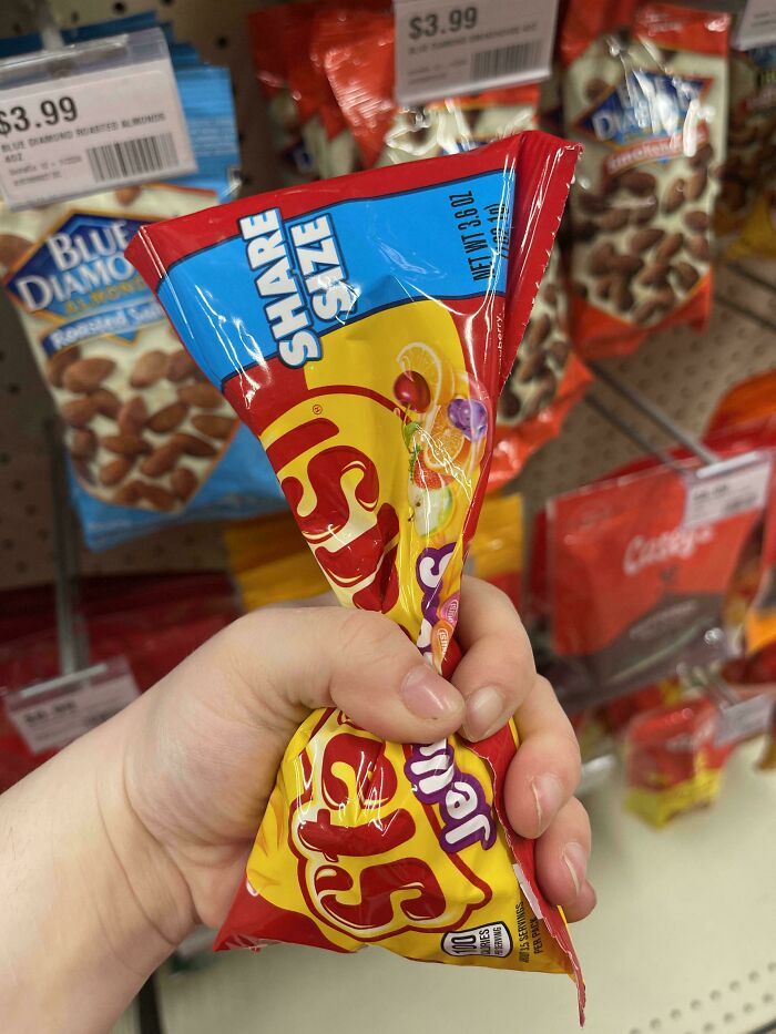 A hand squeezing a half-empty bag of Skittles Share Size candy, depicting infuriating marketing practices with product volume.