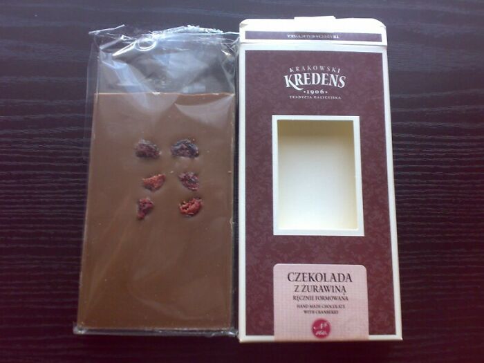 A Krakowski Kredens chocolate bar with only a few cranberries, next to its large box, showing disappointing marketing practices.