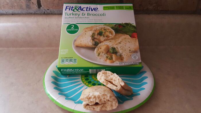 A Fit & Active Turkey & Broccoli Stuffed Sandwich box next to a plate with a sad, flattened sandwich, illustrating misleading marketing practices.