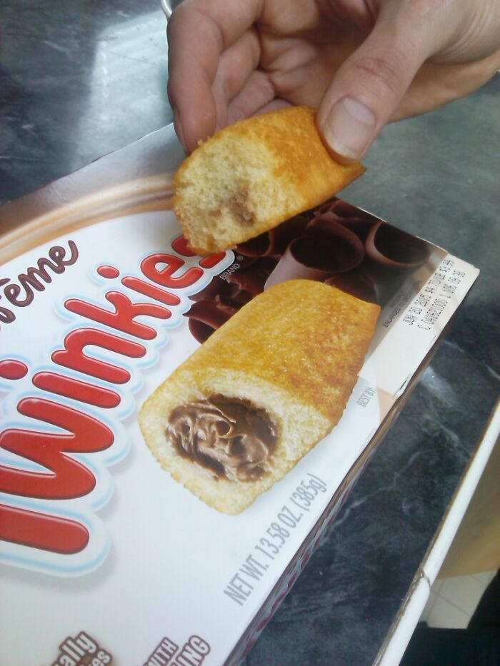 A hand holding a broken Twinkie with minimal chocolate filling, illustrating marketing practices that infuriate consumers.