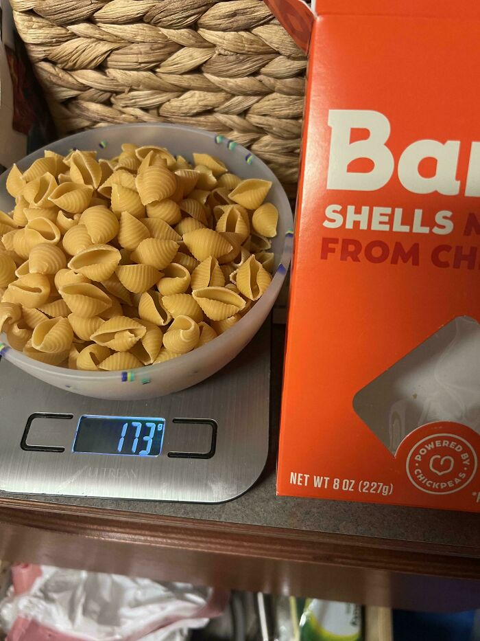 A bowl of pasta shells on a scale, displaying 173 grams next to an 8 oz (227g) box, showing infuriating marketing practices.