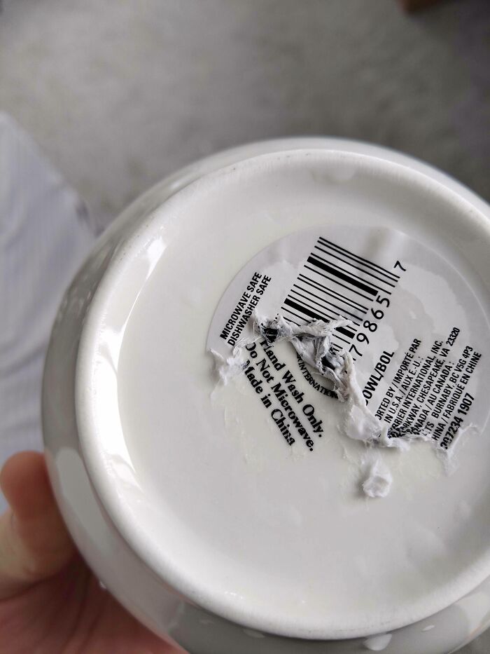 A partially torn label on a ceramic mug, showcasing infuriating marketing practices with conflicting care instructions.