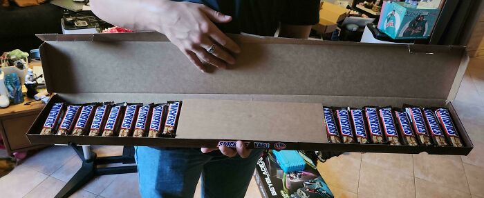 A person holding a long box filled with numerous Snickers candy bars, demonstrating unusual marketing practices.