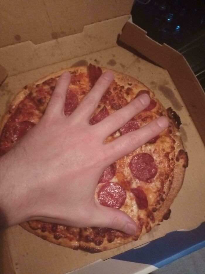 A person's hand covering a small pepperoni pizza in an open box, illustrating misleading marketing practices.