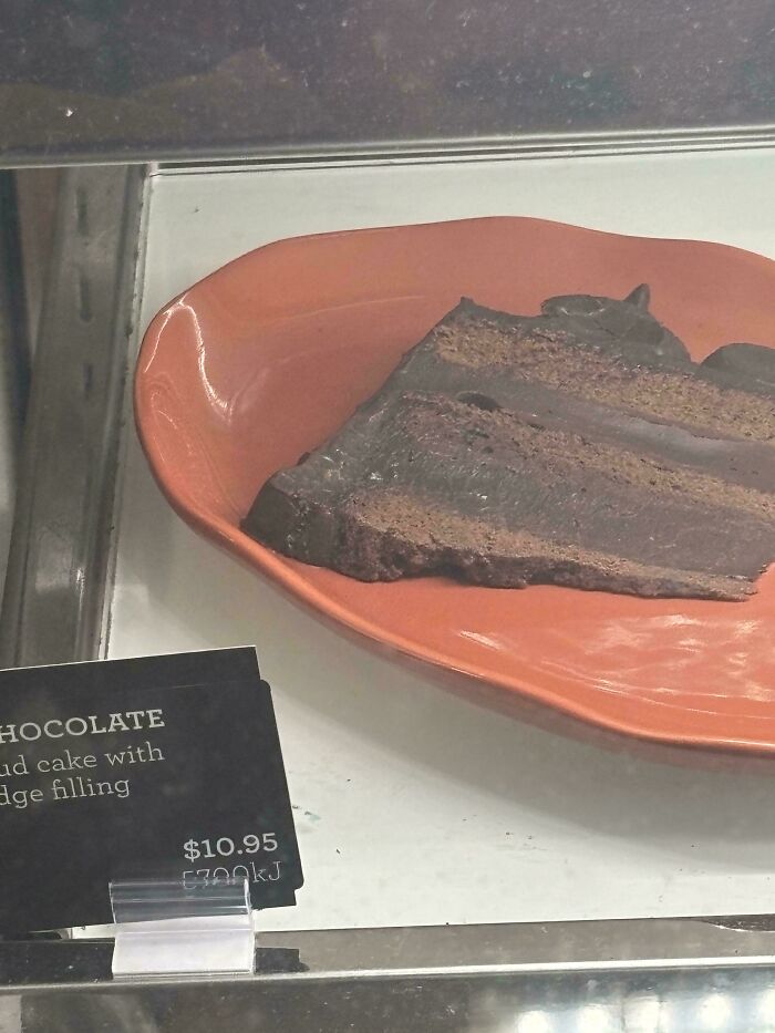 A slice of chocolate mud cake with fudge filling displayed in a case, showing the price and calorie count.
