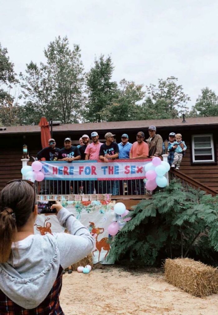 A gender reveal party on a deck, with a banner that reads HERE FOR THE S*X and pink and blue balloons.
