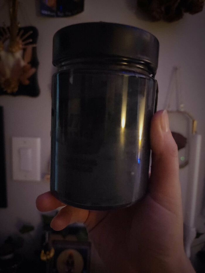 A hand holding a dark jar, reflecting light, in a dimly lit home setting, showing items men found freaky.
