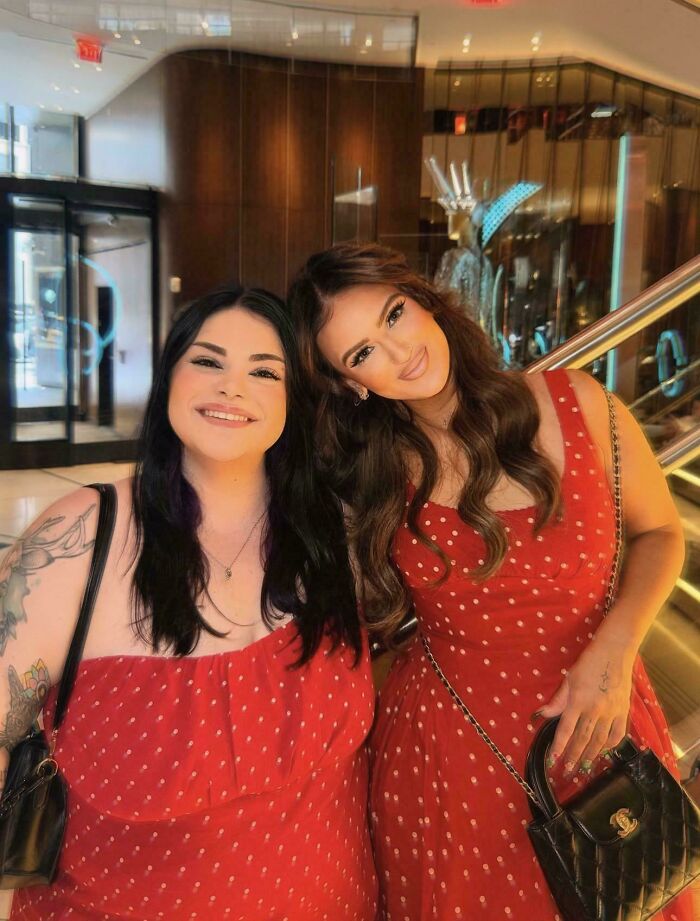 Two women in matching red polka dot dresses smiling together, posing for social media.